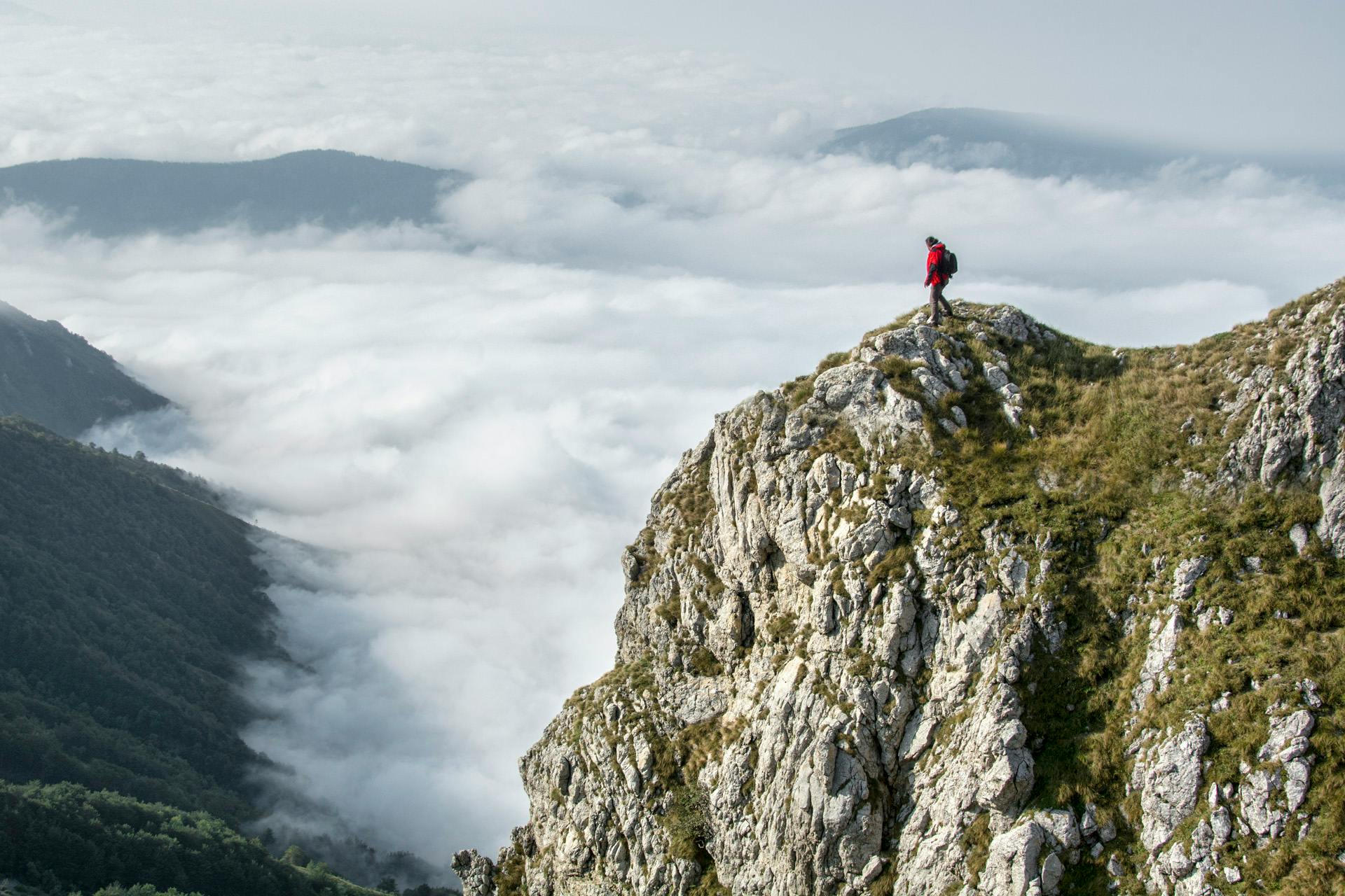 A person is standing at the edge of a cliff overlooking a vast landscape of clouds. Title: 3 Healthy Strategies to Face Your Fears