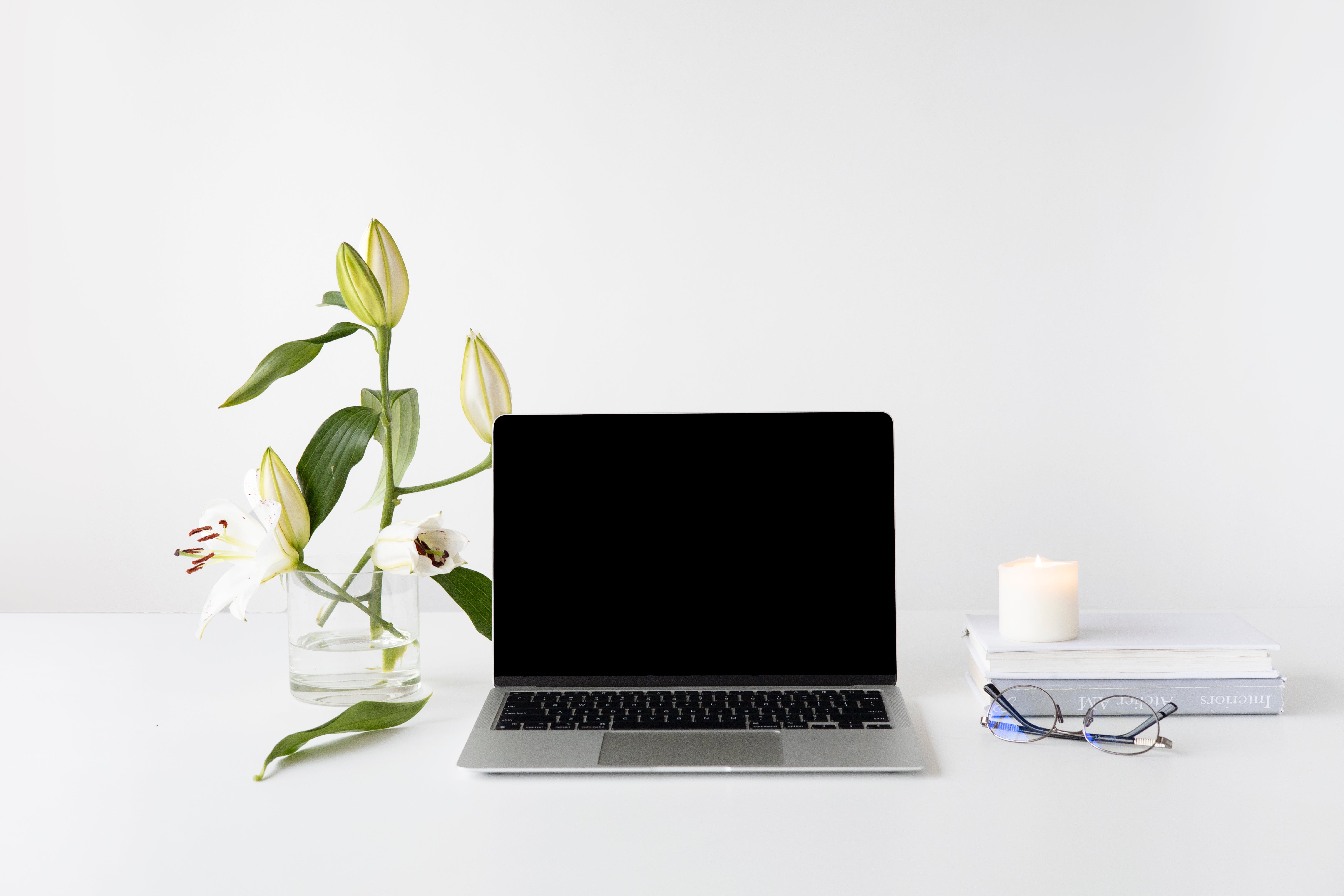 Laptop, flower vase, books and candle arranged neatly on a desk