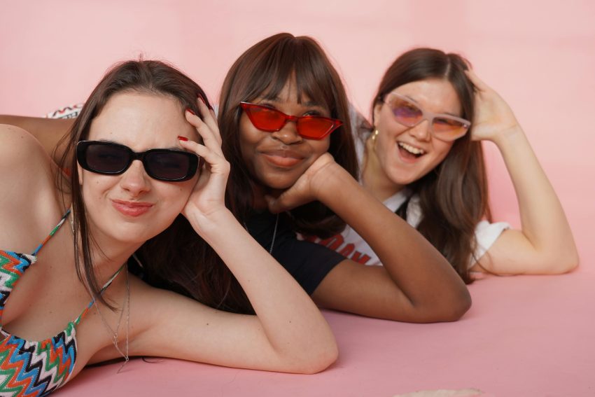 title: tips for maintaining friendships when life is busy. Three women wearing sunglasses lying in a row on the floor and laughing at camera
